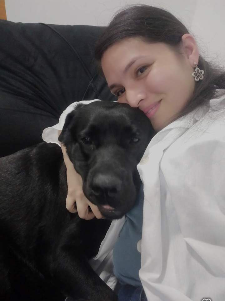 Dra. Oriana abraçando um cachorro preto no sofá de casa
